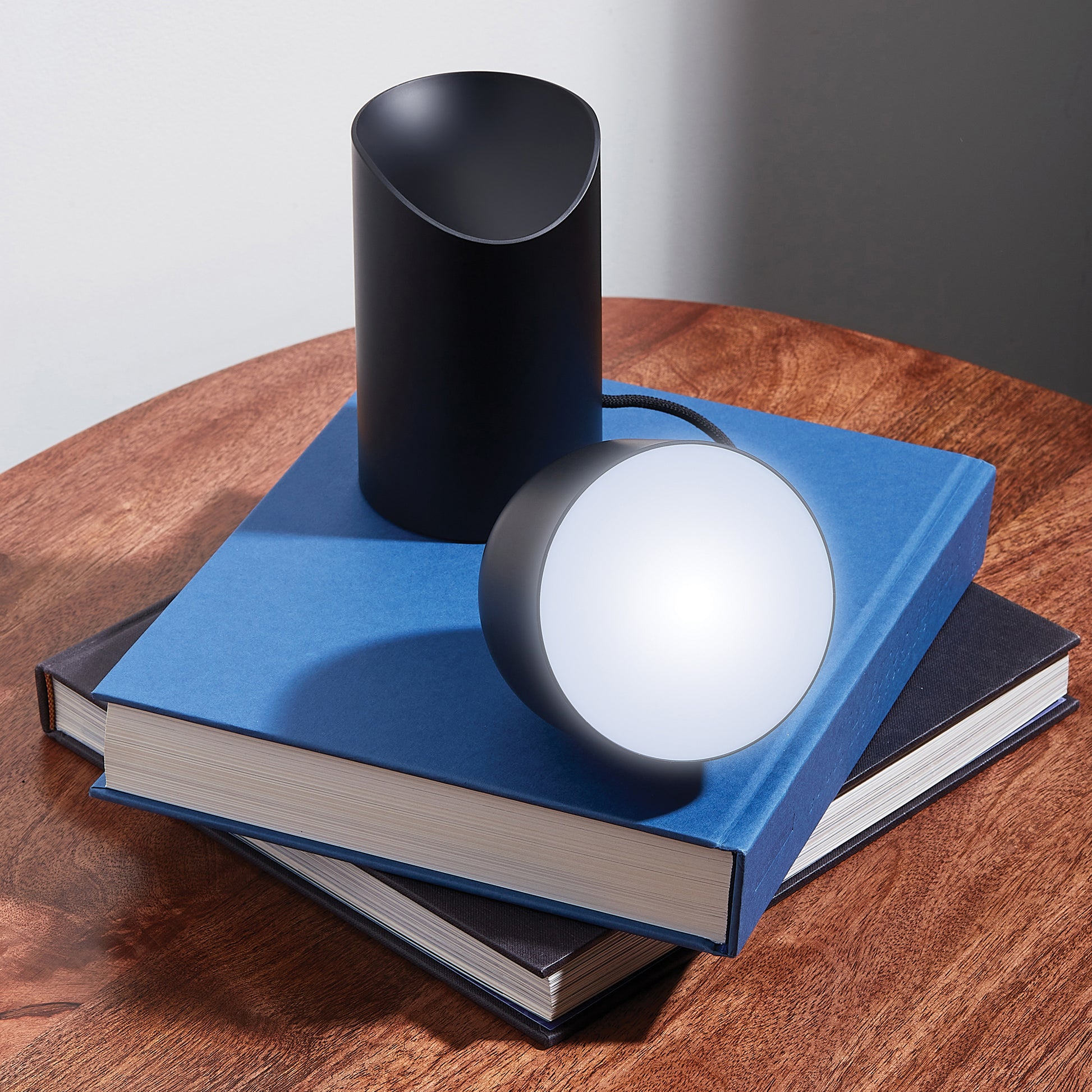 Lexon Orbe Zwart│Oplaadbare Tafellamp│art. LH88N│op stapel boeken met lamphoofd los
