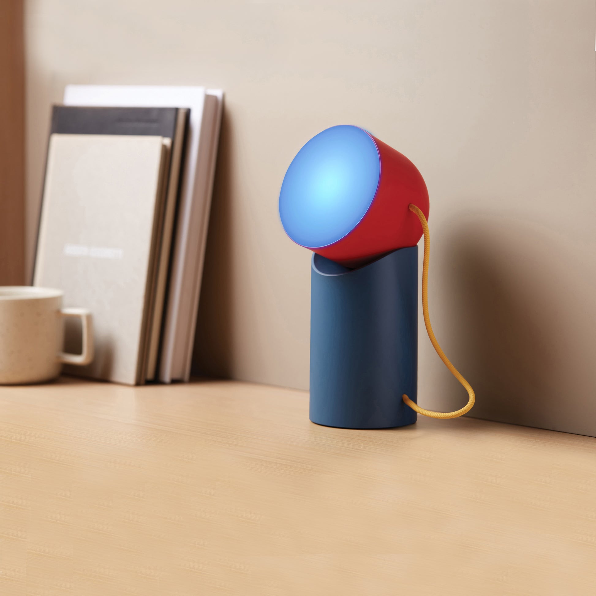 Lexon Orbe Duck Blue&Red│Oplaadbare Tafellamp│art. LH88DRY│op houten plank naast boeken met blauw licht aan