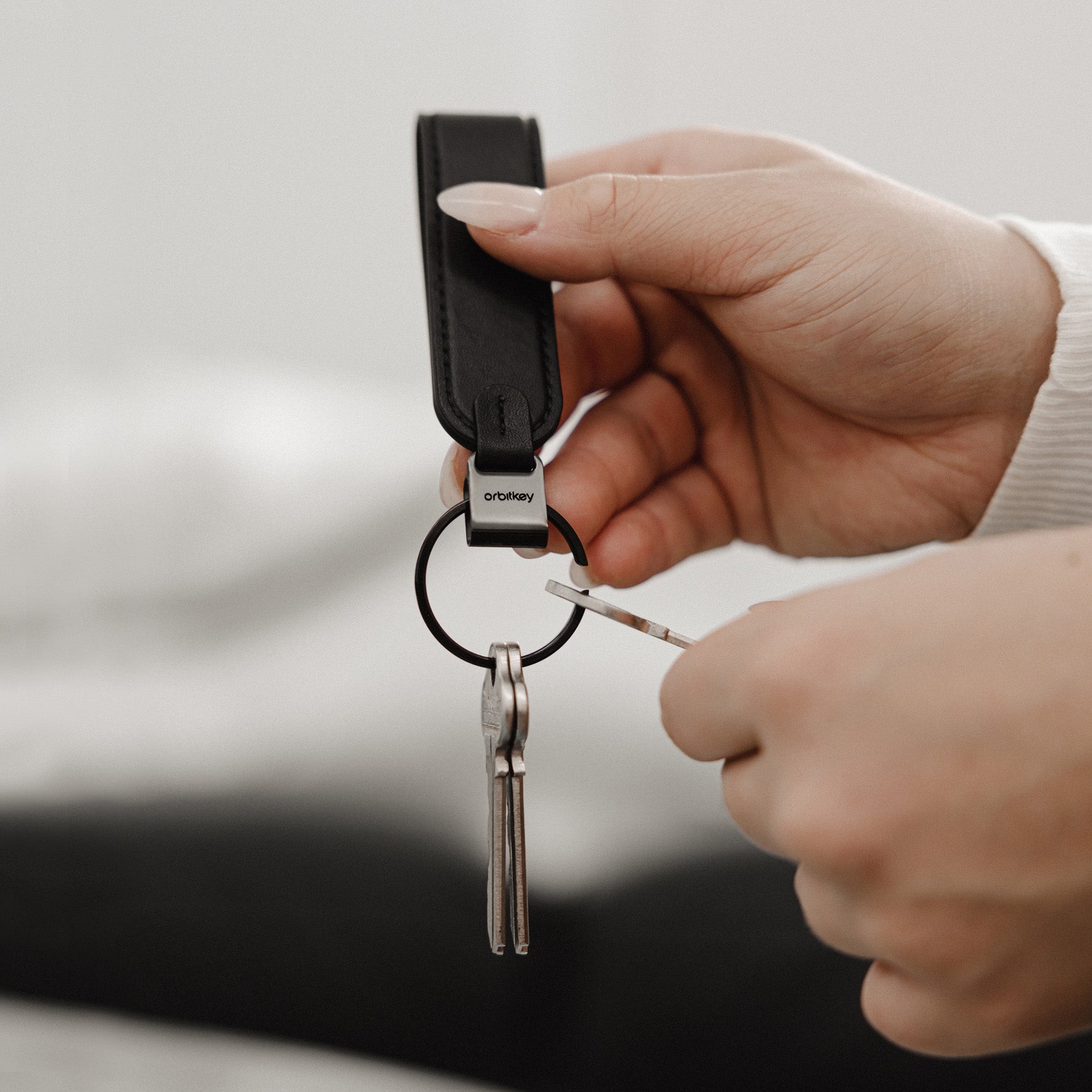 Orbitkey LoopZwart│Sleutelhange Leer│art. PLK1-BLK-101│met handen die sleutel toevoegen
