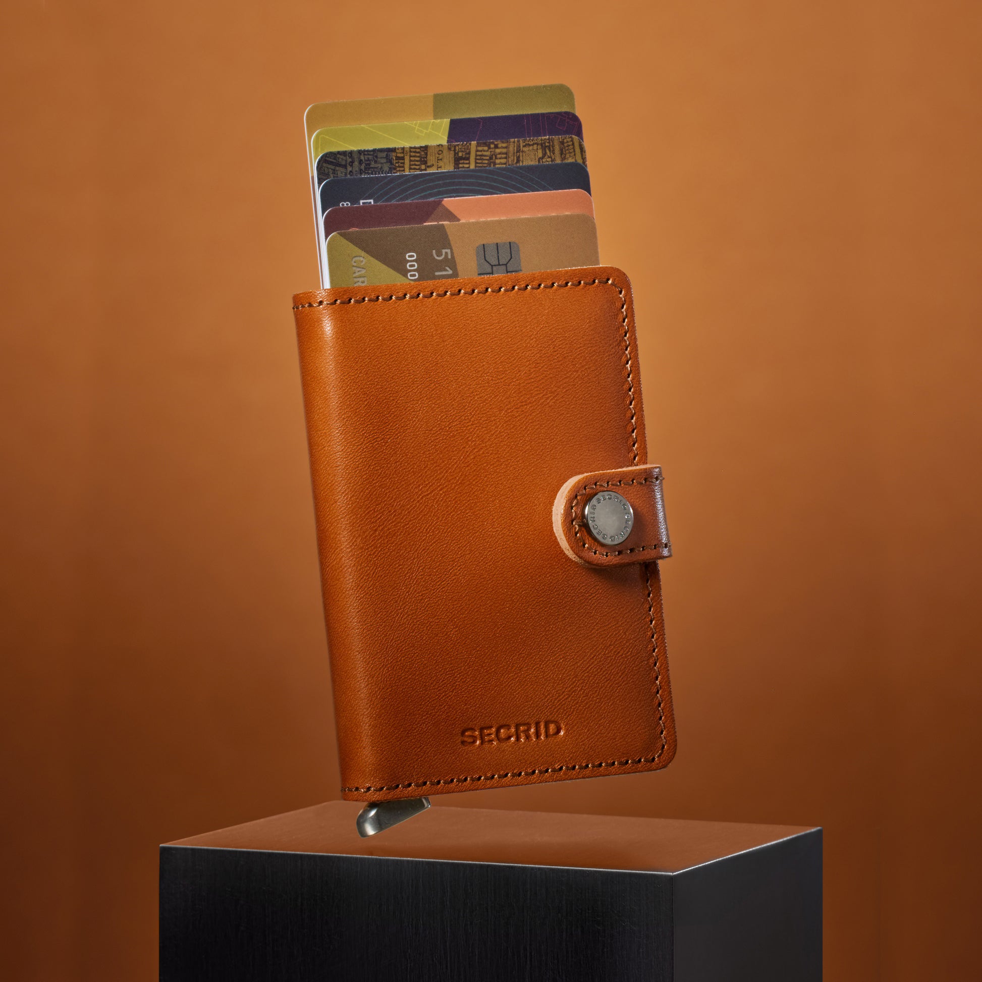 Secrid Miniwallet Premium Basco│Pasjeshouder│art. MBC-COGNAC│zwevend boven kubus met beige achtergrond