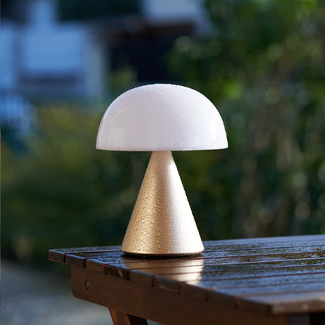 Lexon Mina Large Oplaadbare Tafellamp Goud│art. LH65MD│op buitentafel met regendruppels