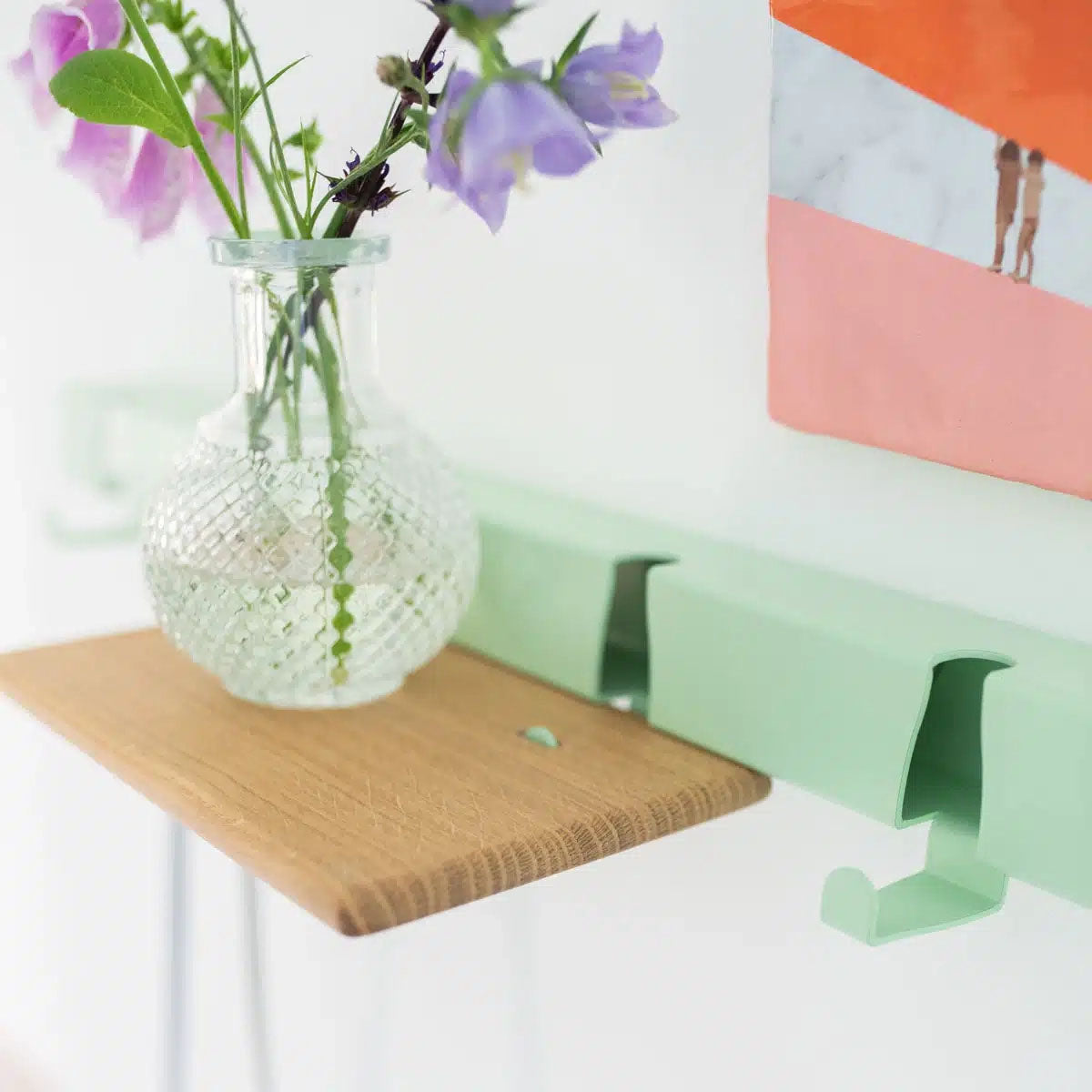 Eiken plankje met glazen vaasje hangt aan Wandkasptok Coatrack by the Meter van Vij5 in Mintgroen