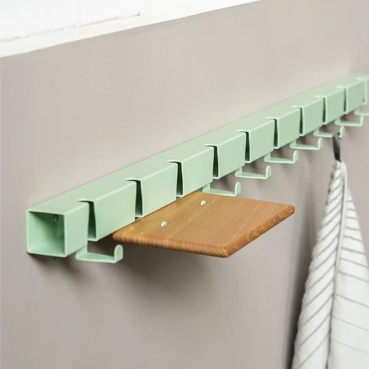Wandkapstok Coatrack by the Meter hangt tegen beige wand met eiek plankje en theedoek aan haakje
