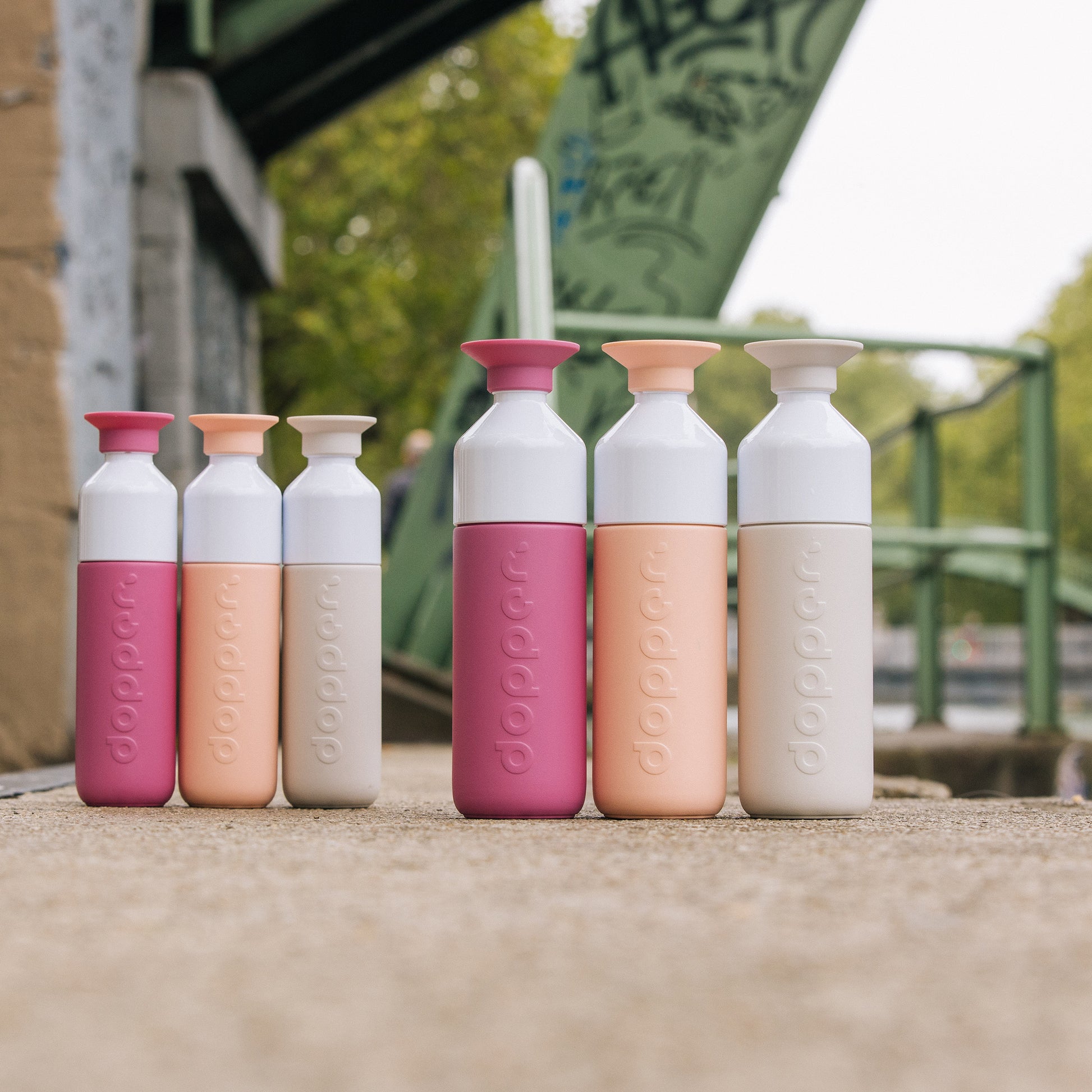 Dopper Insulated Small en large in diverse kleuren naast elkaar met ijzeren brug op achtergrond