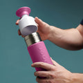 man plaatst dop van Dopper Insulated Small Pelican Pink (Thermosfles roze) - op fles met groene achtergrond