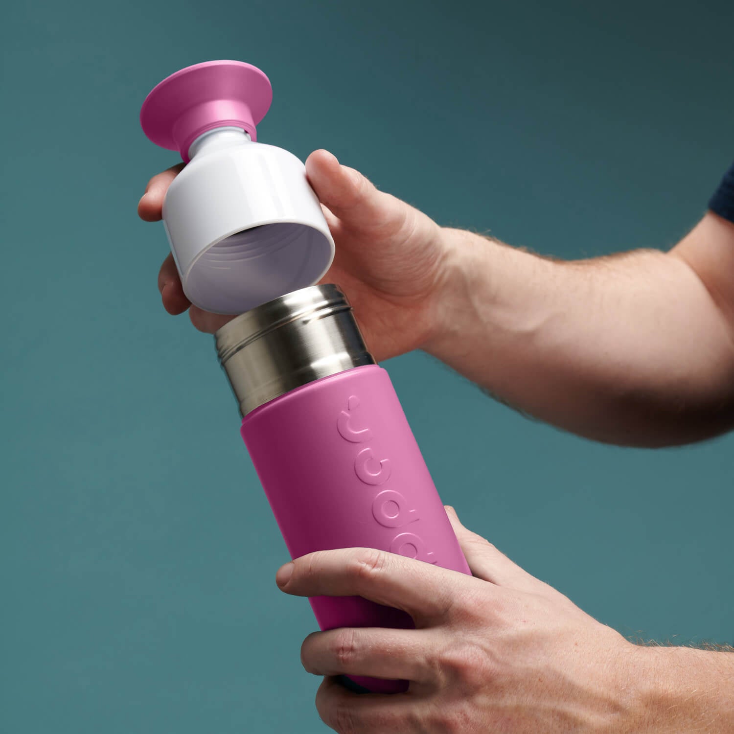 man plaatst dop van Dopper Insulated Small Pelican Pink (Thermosfles roze) - op fles met groene achtergrond
