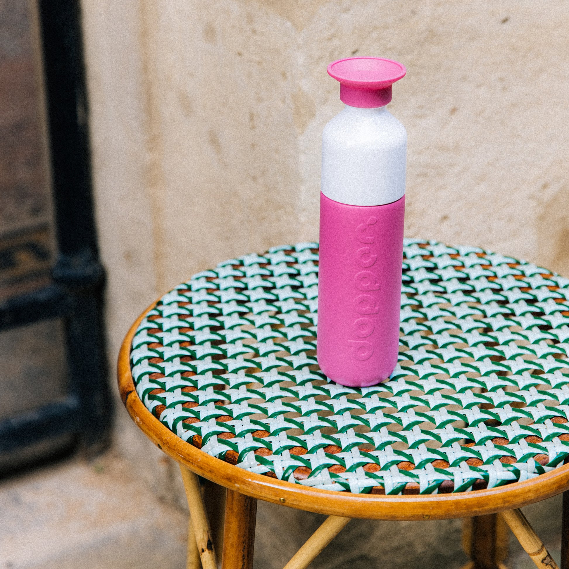 Dopper Insulated Small Pelican Pink( Thermosfles roze) staat op rieten terrastafeltje