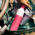 vrouw legt Dopper Insulated Small Pelican Pink( Thermosfles roze) in fietsmand naast Susan Bijl tas