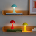 Remember Filou Oplaadbare LED Tafellamp | in drie kleuren met het licht aan op houten planken met boeken
