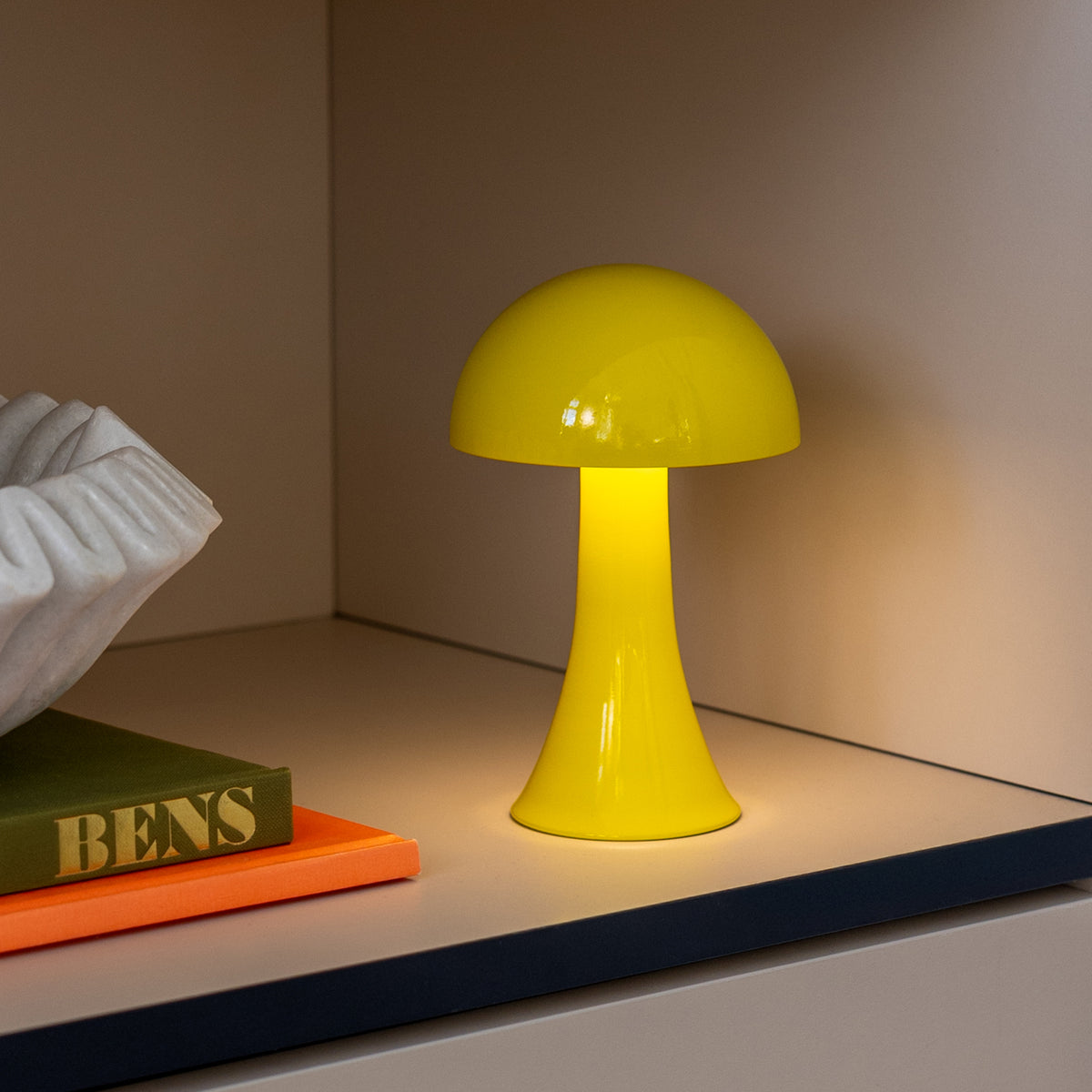 Remember Filou Oplaadbare LED Tafellamp | Geel | art. LLM01 | in een kast naast boeken en een schaal, licht aan