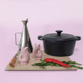 Gluckigluck salt and pepper shakers in pink on a chopping board beside a pan and kitchen utensils.