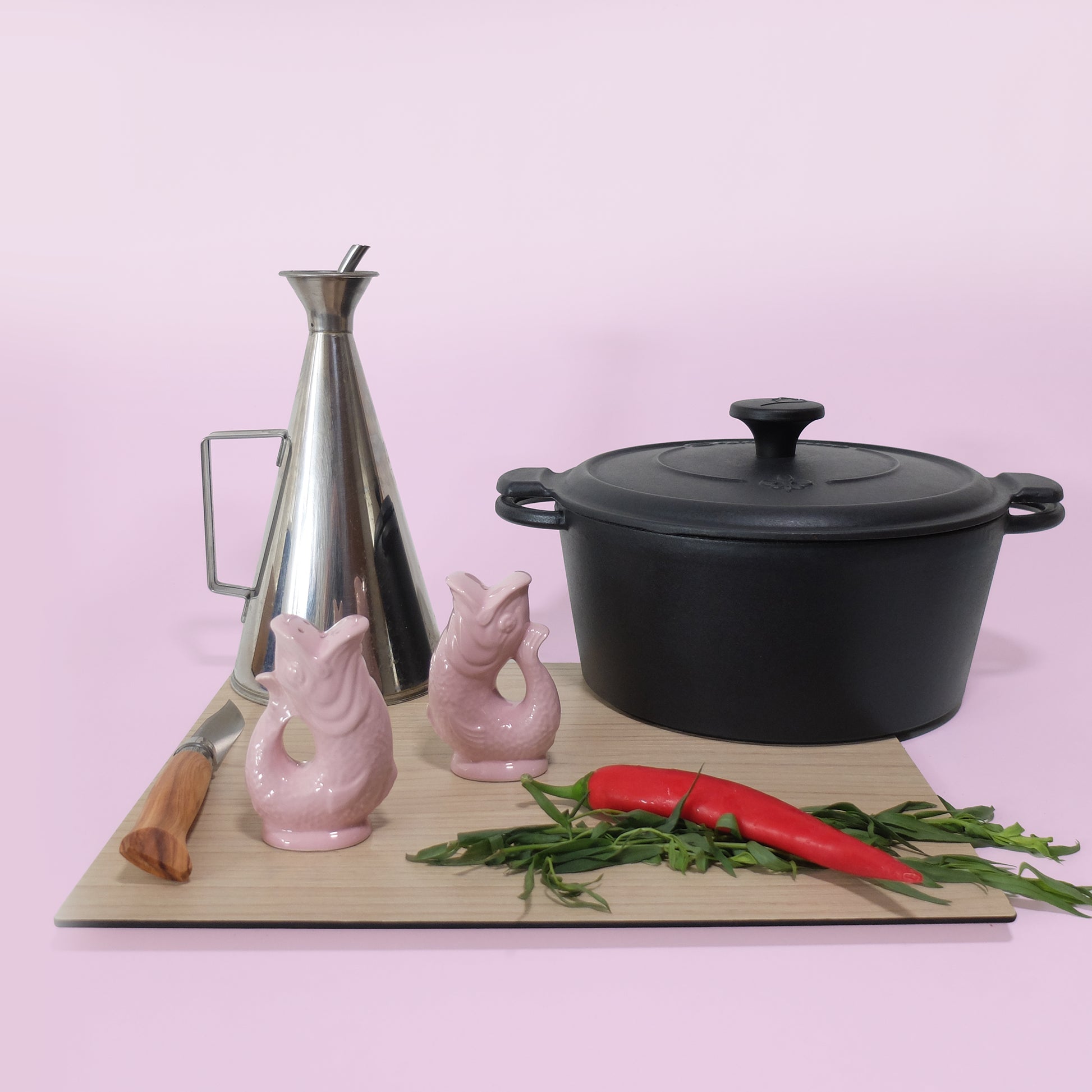 Gluckigluck salt and pepper shakers in pink on a chopping board beside a pan and kitchen utensils.