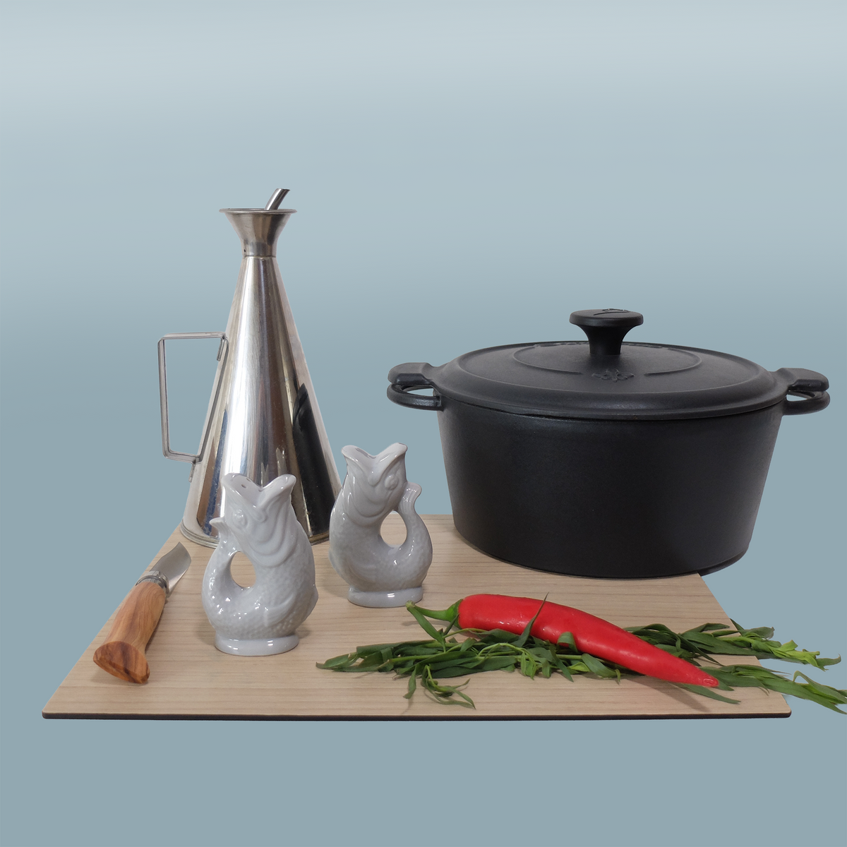 Gluckigluck salt and pepper shakers in Oyster on a chopping board beside a pan and kitchen utensils.