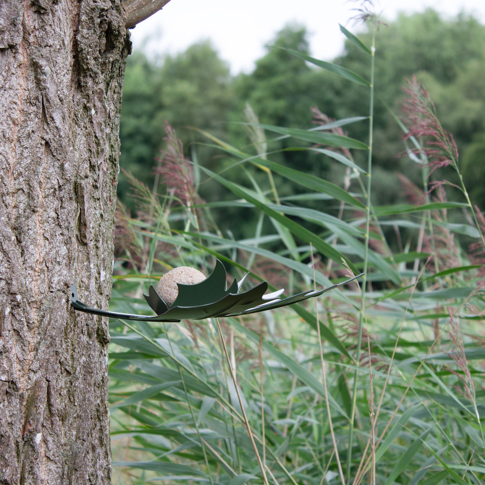 zijaanzicht van Birdfeeder Leaf Me Groen van Heeej tegen een dikke boom bevestigd.