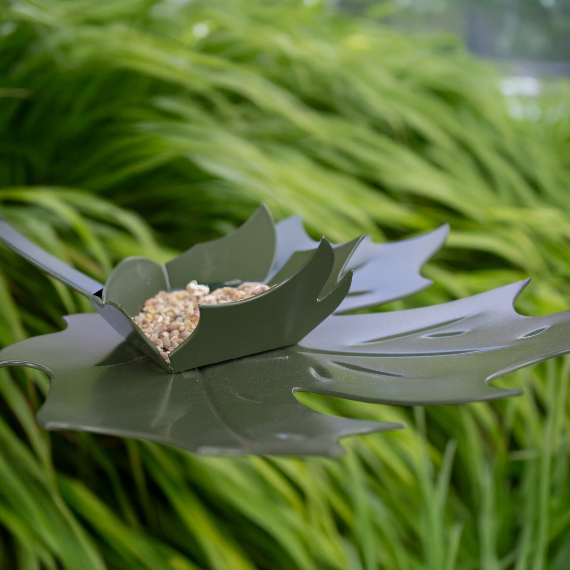 Close-up van Birdfeeder Leaf Me - Groen metalen blad in de vorm van een plataan met gras op achtergrond