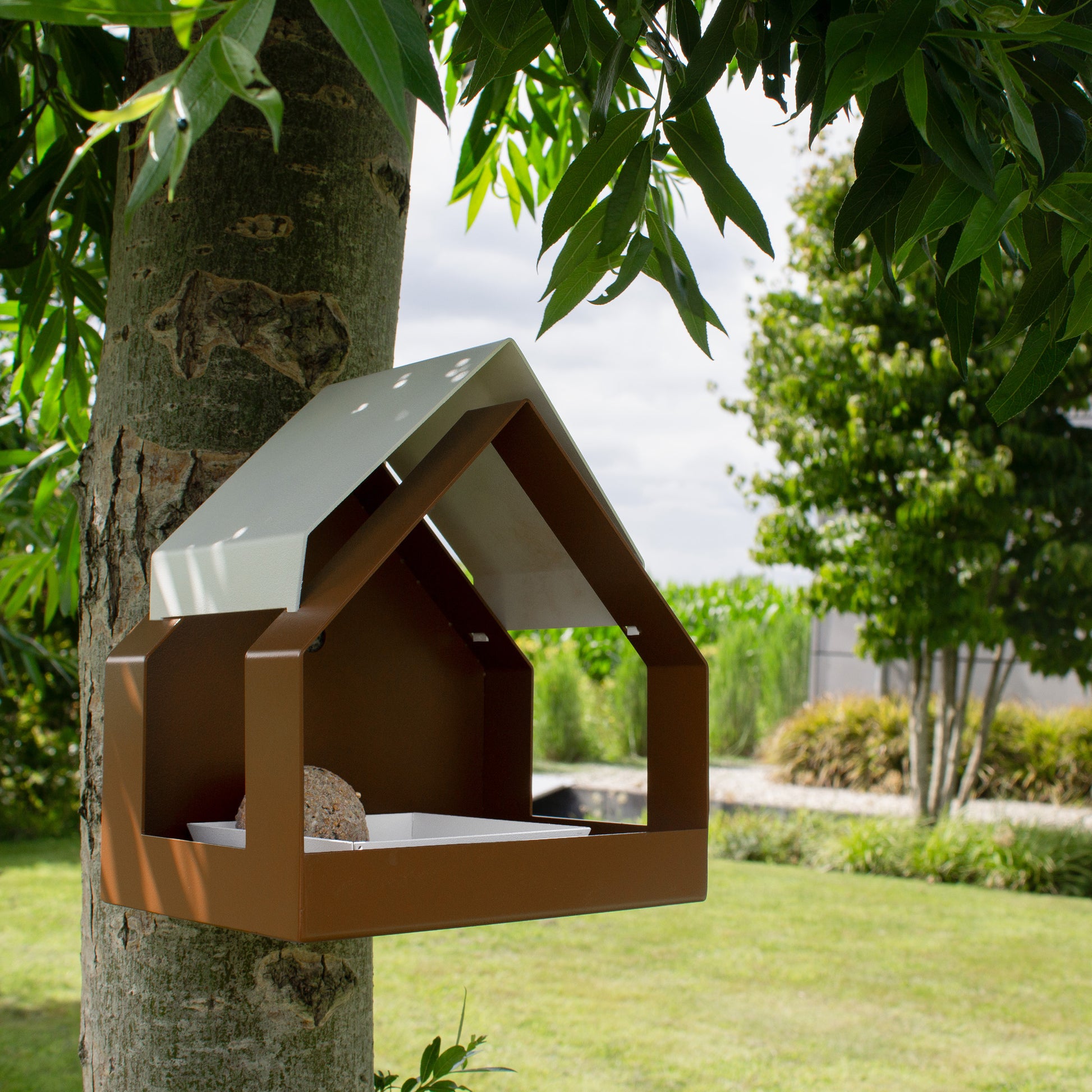 Wandvogelvoederhuis The Barn van Heeej hangt aan een boom in een moderne tuin
