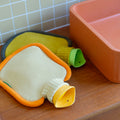 Warmwaterkruik Mini Bumper van Suite702 in de kleur Clementine en Mustard liggend op houten badkamermeubel naast oranje wasbak