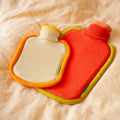 Warmwaterkruik Mini Bumper Clementine en Bumper in Poppy Orange liggen op geel dekbed