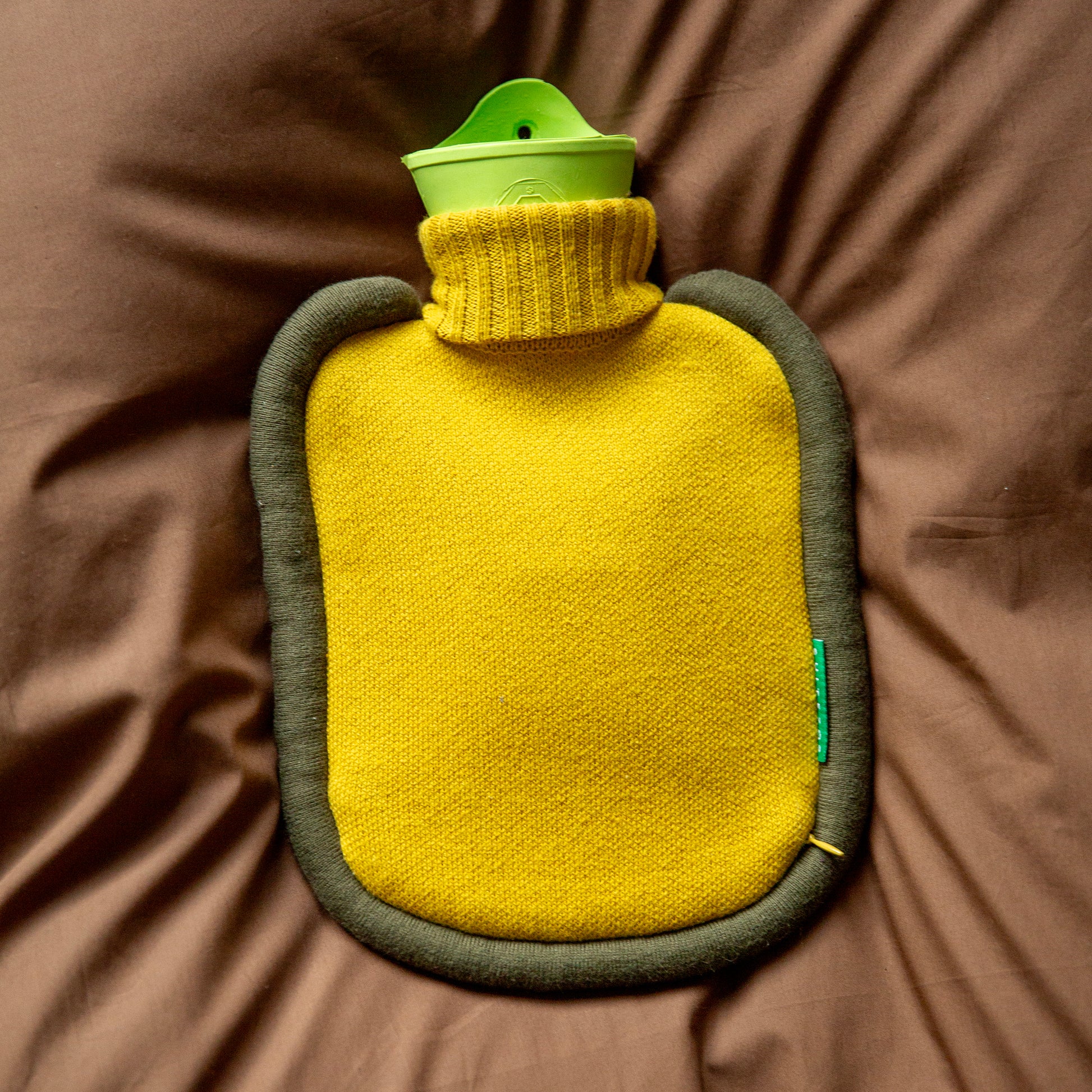 Bovenaanzicht Warmwaterkruik Mini Bumper Mustard van Suite702 liggend op bruin dekbed