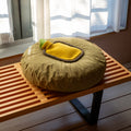 Warmwaterkruik Mini Bumper Mustard van Suite702 - liggend op rond kussen op houten bankje voor raam