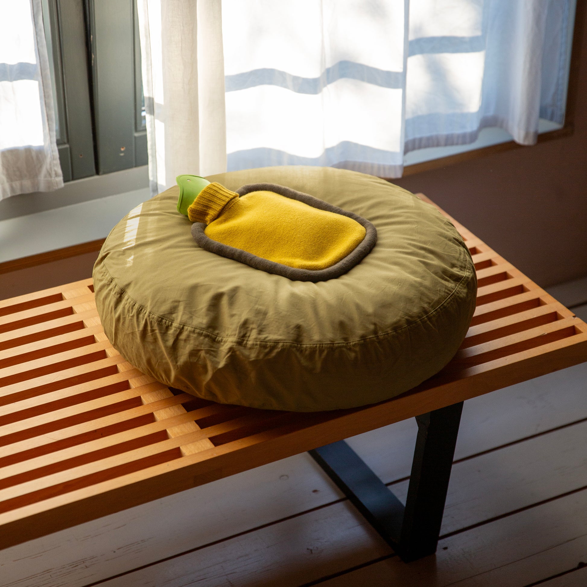 Warmwaterkruik Mini Bumper Mustard van Suite702 - liggend op rond kussen op houten bankje voor raam