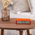 Lexon Flip+ Wekker Digitaal Oranje│art. LR157O4│op rond houten tafeltje met verlichting uit