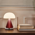 Lexon Mina Large Oplaadbare Tafellamp Donkerrood│art. LH65DR│op oplader met licht aan naast boeken