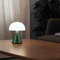 Lexon Mina Large in donkergroen op een houten salontafel met het licht aan