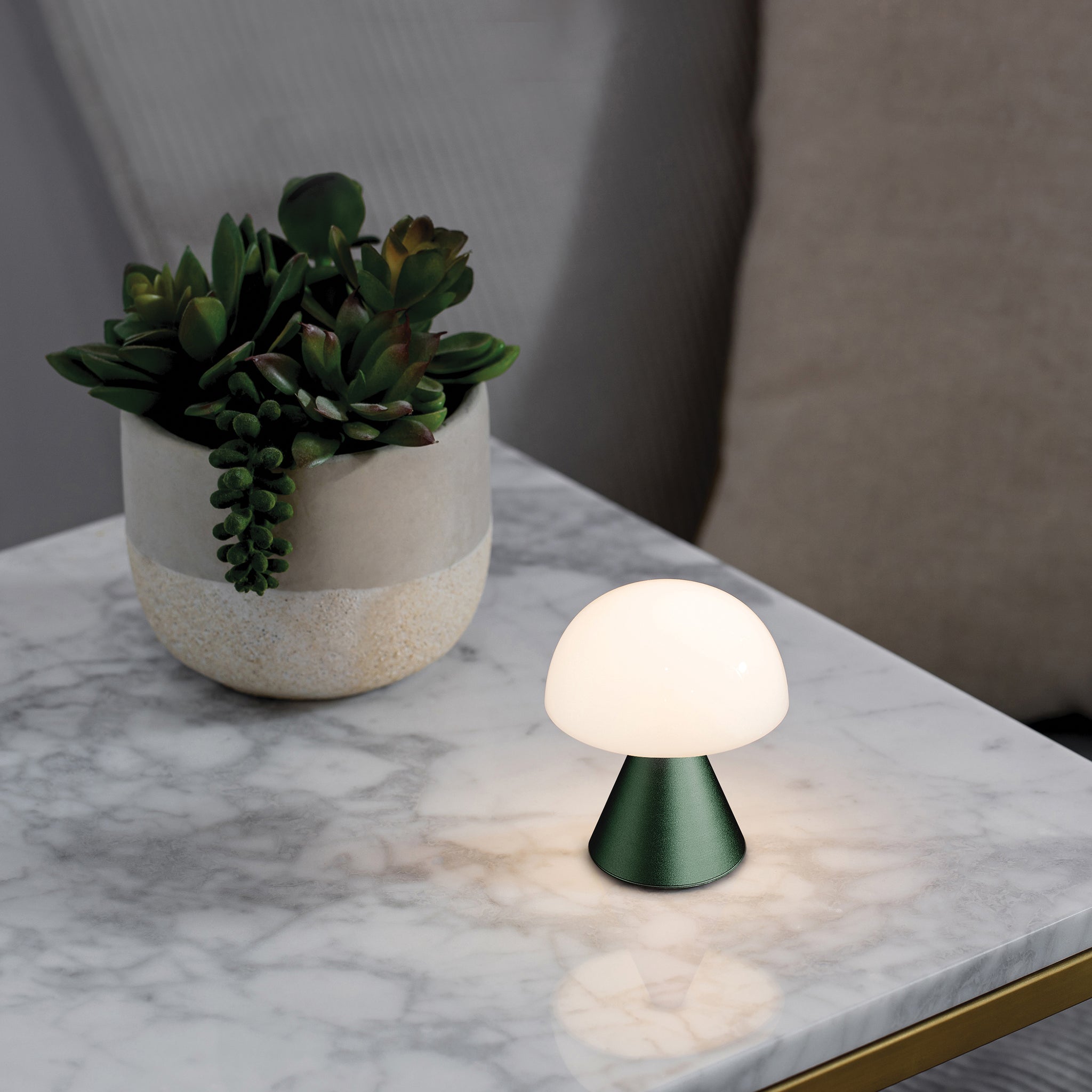 Lexon Mina Small Oplaadbare LED-Lamp Donkergroen│art. LH60DG1│op tafeltje naast plant met licht aan