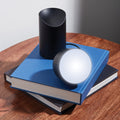 Lexon Orbe Zwart│Oplaadbare Tafellamp│art. LH88N│op stapel boeken met lamphoofd los