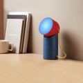 Lexon Orbe Duck Blue&Red│Oplaadbare Tafellamp│art. LH88DRY│op houten plank naast boeken met blauw licht aan