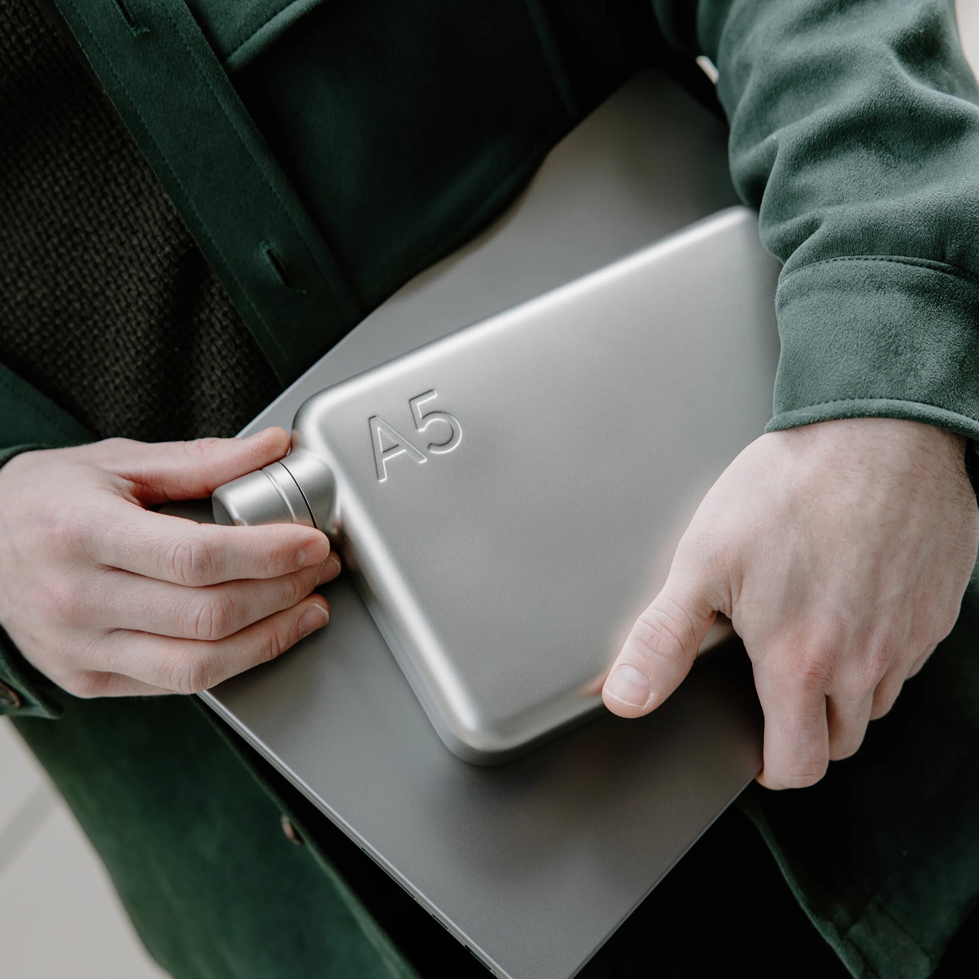 Man houdt Memobottle A5 Stainless Steel RVS satijn in hand samen met laptop.