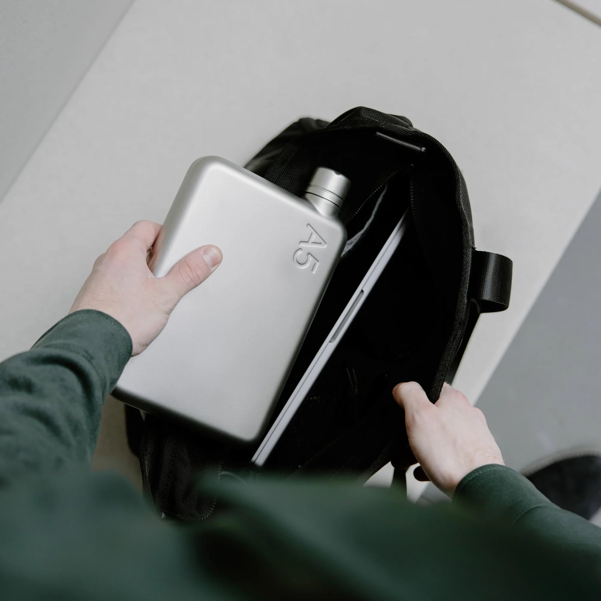Man stopt Memobottle A5 Satin RVS in tas naast laptop.