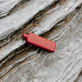Memobottle Slim platte waterfles RVS rood, liggend op een stenen ondergrond in de natuur.