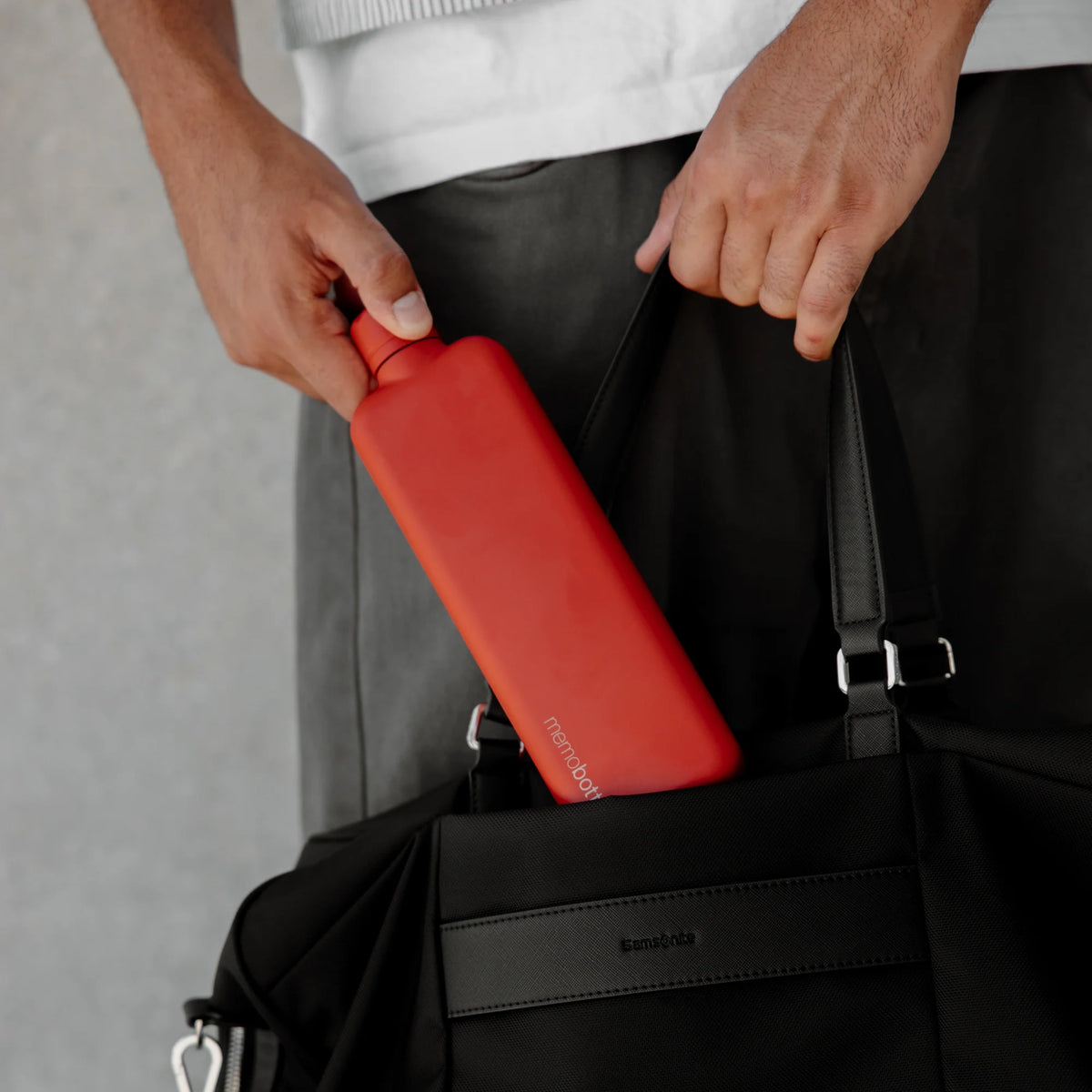 Man stopt de Memobottle Slim platte waterfles RVS rood in een zwarte tas.