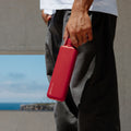 Man houdt de Memobottle Slim platte waterfles RVS rood bij de dop in zijn hand.
