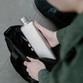 Man stopt Memobottle Platte Waterfles Slim RVS Slim Satin in zwarte tas.