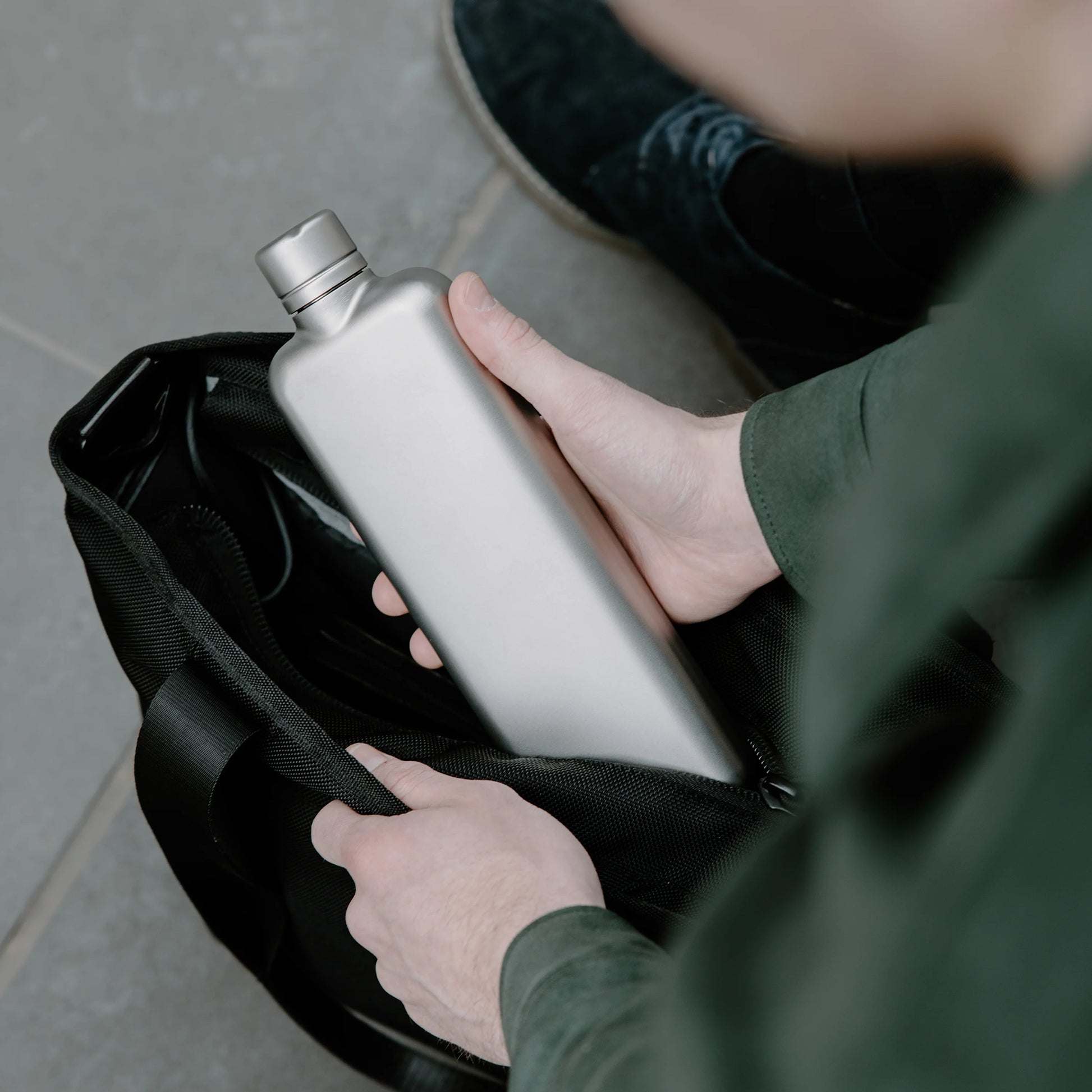 Man stopt Memobottle Platte Waterfles Slim RVS Slim Satin in zwarte tas.