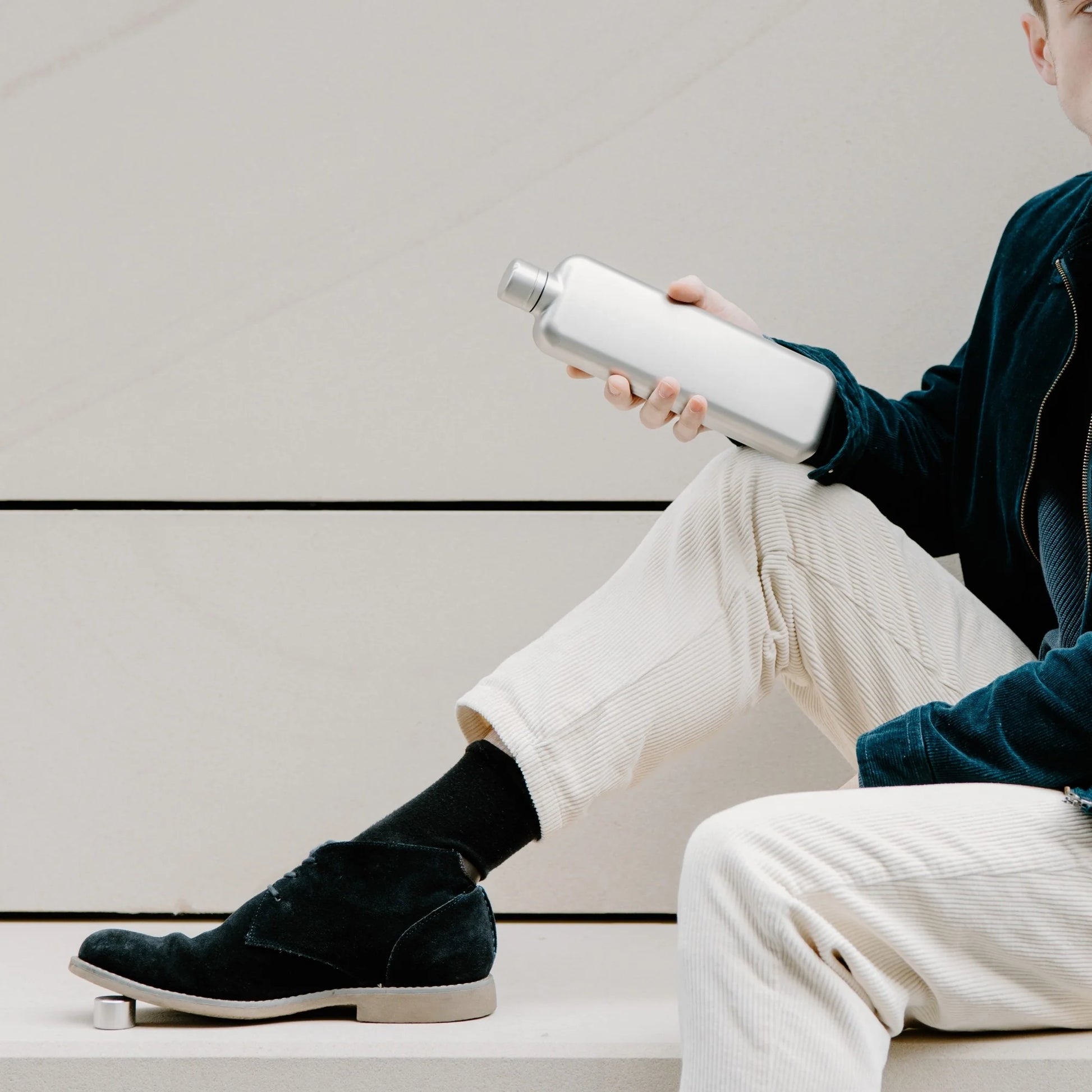 Man op betonnen bank houdt Memobottle Platte Waterfles Slim RVS Slim Satin in hand.
