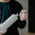 Memobottle Platte Waterfles Slim RVS Slim Satin in hand met dop in andere hand.