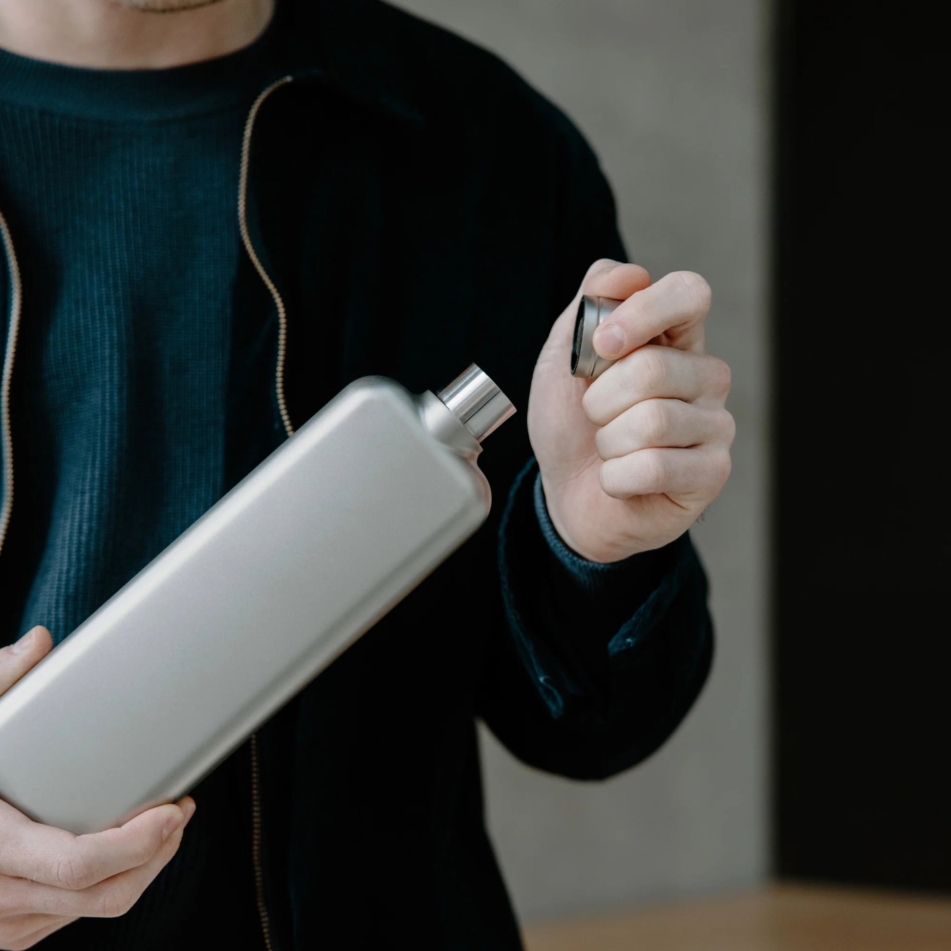 Memobottle Platte Waterfles Slim RVS Slim Satin in hand met dop in andere hand.