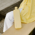 Memobottle Slim flat stainless steel water bottle in yellow on a woman's leg on a concrete ledge.
