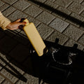 Woman putting the Memobottle Slim flat stainless steel water bottle in yellow into her bag outdoors.