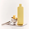 Memobottle Slim flat stainless steel water bottle in yellow on an iron tray with small bowls and a pair of tongs.