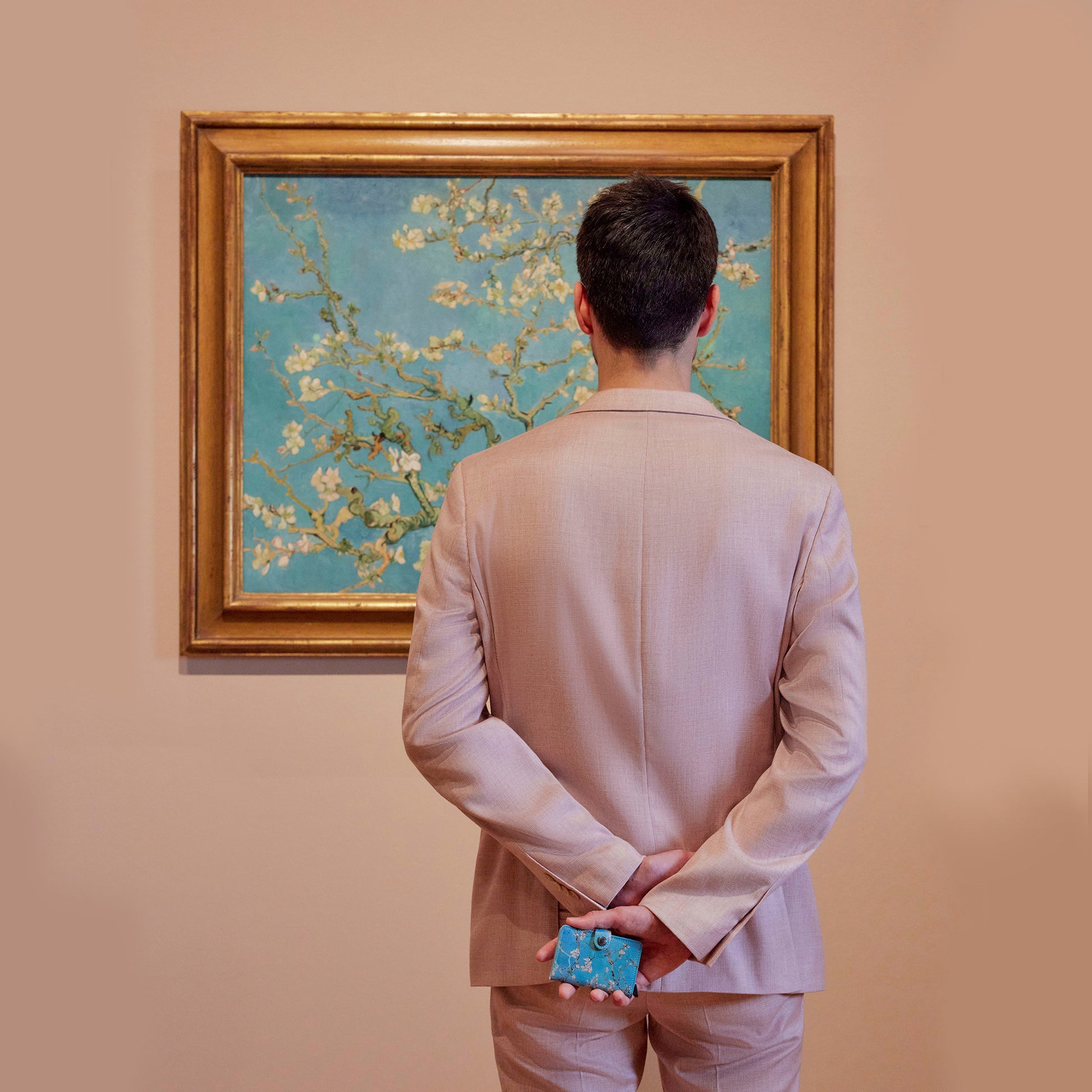 Secrid Miniwallet Art Collection│art. MAR-ALMOND BLOSSOM│man voor schilderij met portemonnee in handen op zijn rug