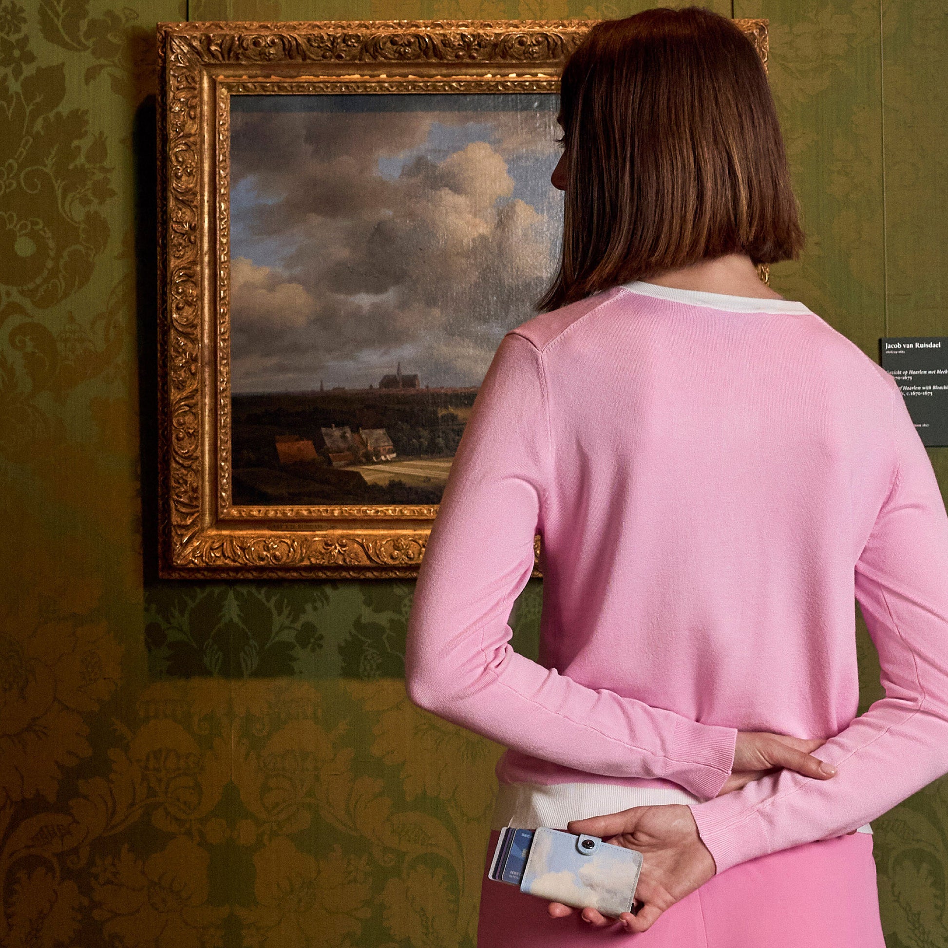 Secrid Miniwallet Art Collection│art. MAR-CLOUDS│vrouw voor schilderij met portemonnee in hand