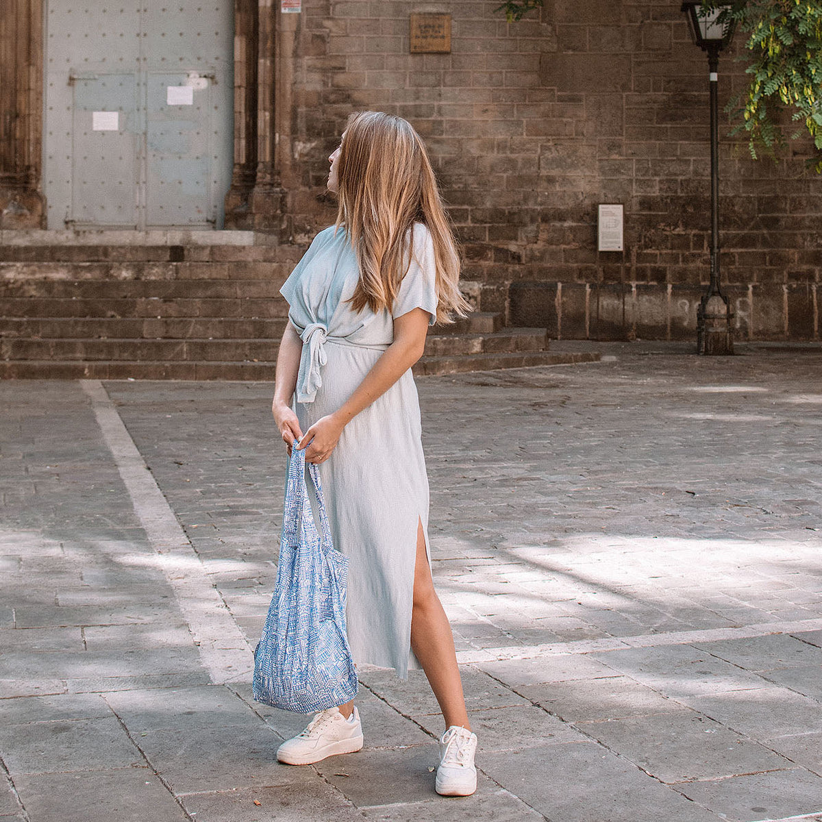 Vrouw draagt Notabag Hello World Raw Blue shopper op een pleintje voor een kerk