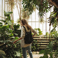 Frau trägt Notabag Recycled Schwarz Rucksack bei tropischen Pflanzen in einem Innenhofgarten