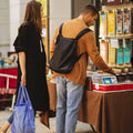 Mann mit Notabag Recycled Schwarz Rucksack und Frau mit Shopper-Tasche in einem Geschäft