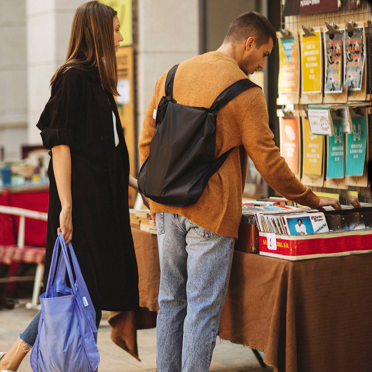 Mann mit Notabag Recycled Schwarz Rucksack und Frau mit Shopper-Tasche in einem Geschäft